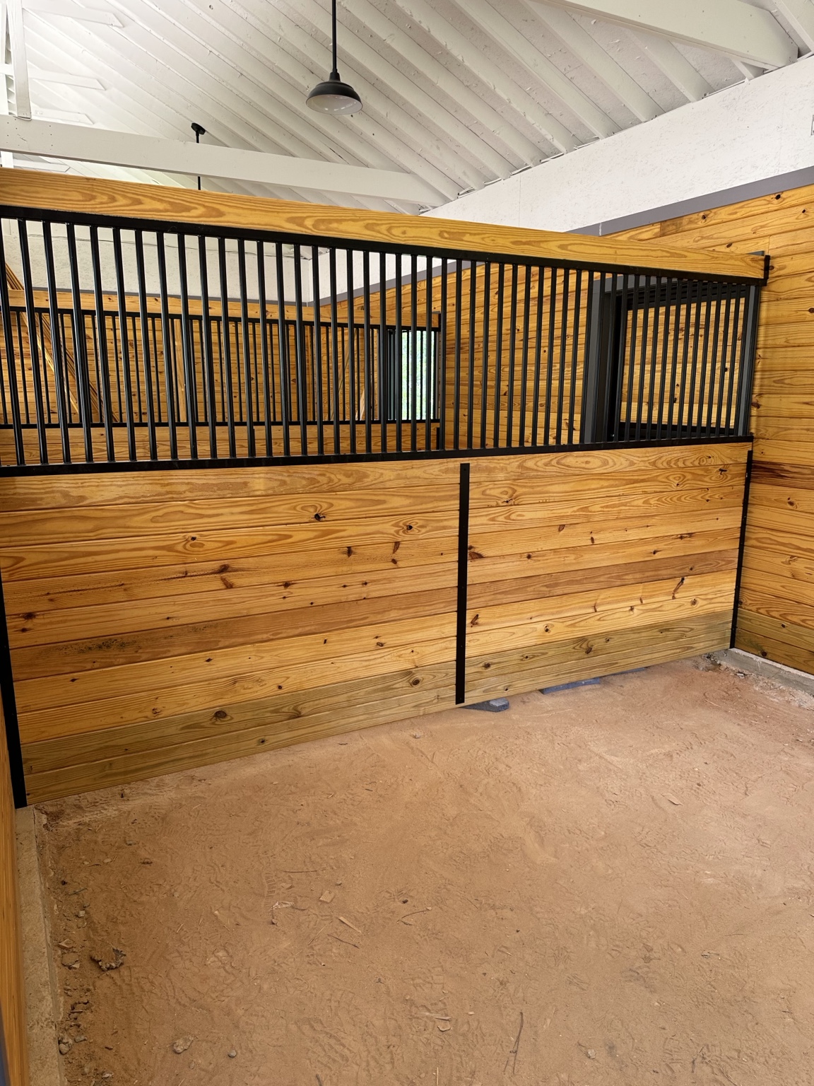 Custom horse stall with warm wood plank walls, black steel framing, and closely spaced upper bars