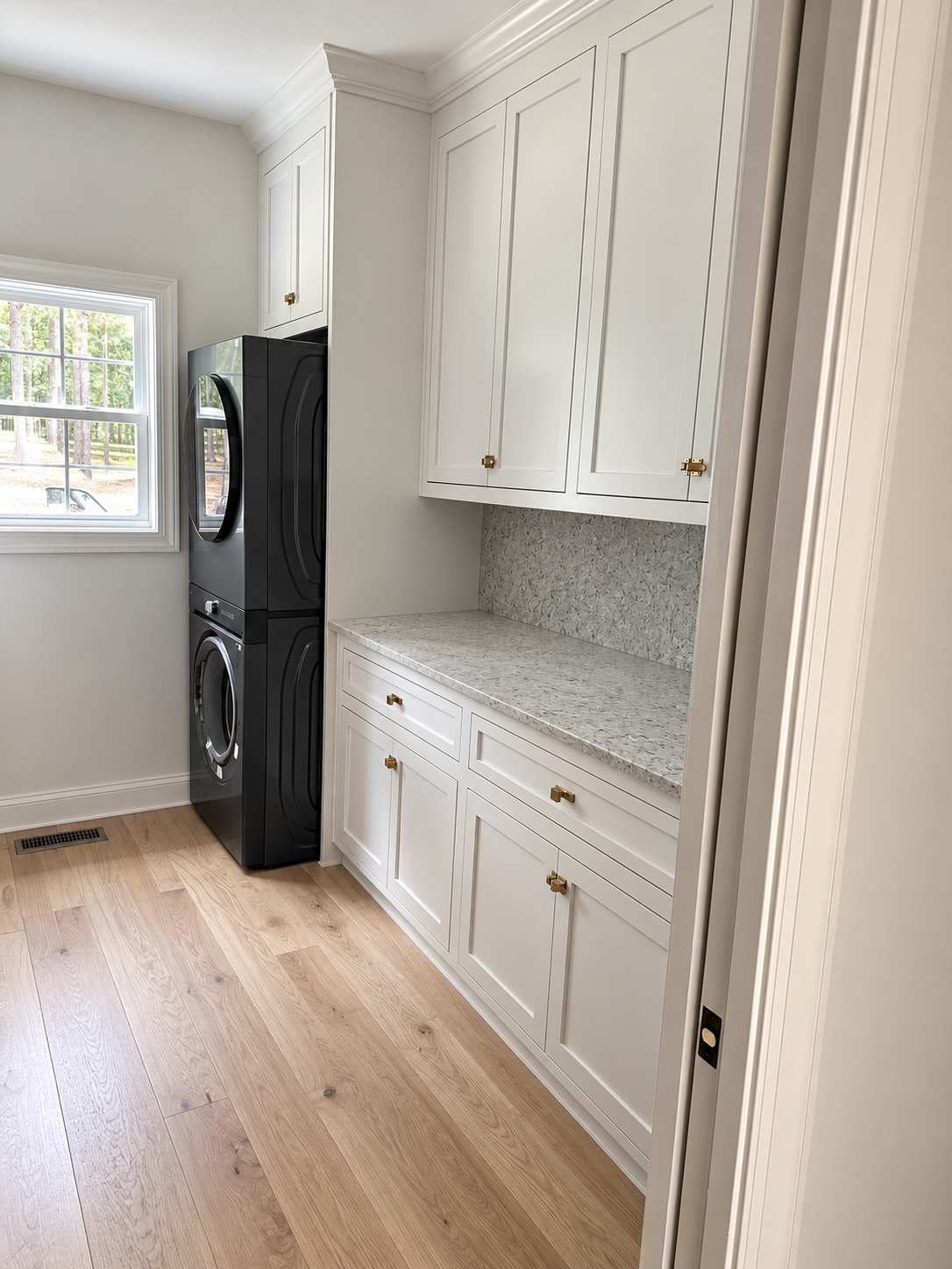 Laundry room with white full-height cabinetry, stone counter, brass hardware, and black stacked machines