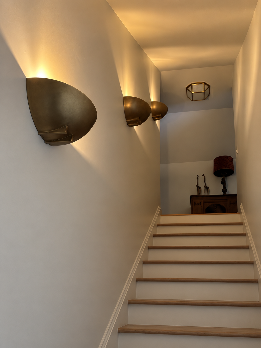Warm narrow stair hall with oak treads, white risers, and sculptural bronze wall lights